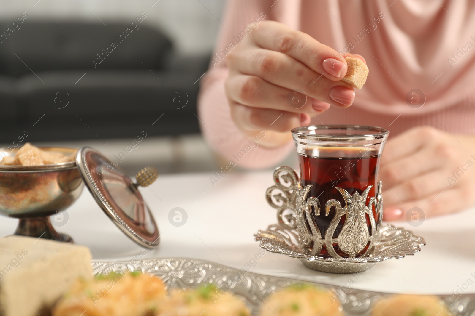 Photo of Woman adding sugar to delicious Turkish tea at white table, closeup