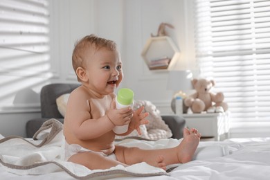Adorable little baby with bottle of dusting powder on bed at home, space for text