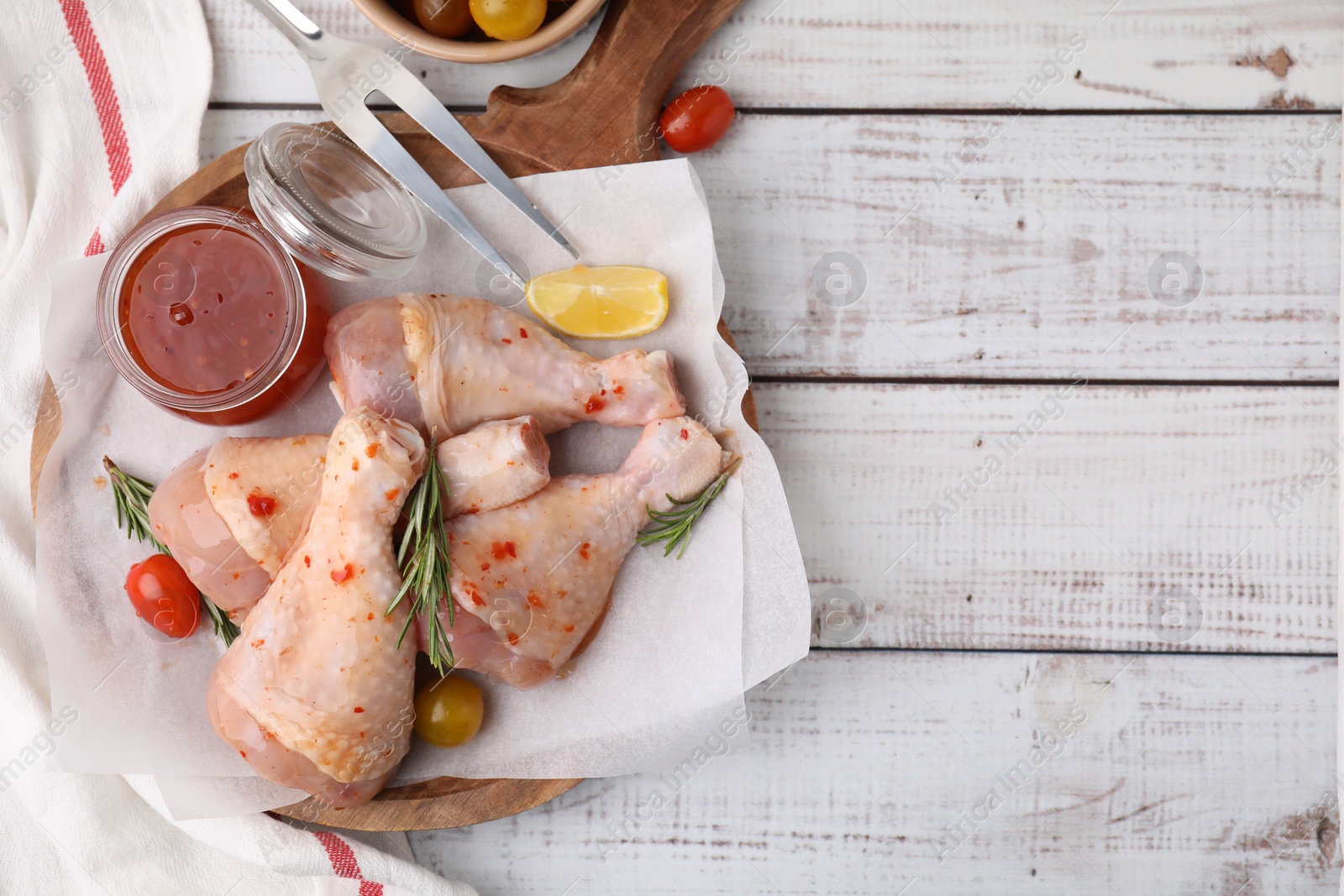 Photo of Marinade, raw chicken drumsticks, tomatoes and rosemary on white wooden table, flat lay. Space for text