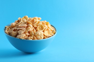 Photo of Bowl of tasty crispy corn flakes on light blue background, space for text