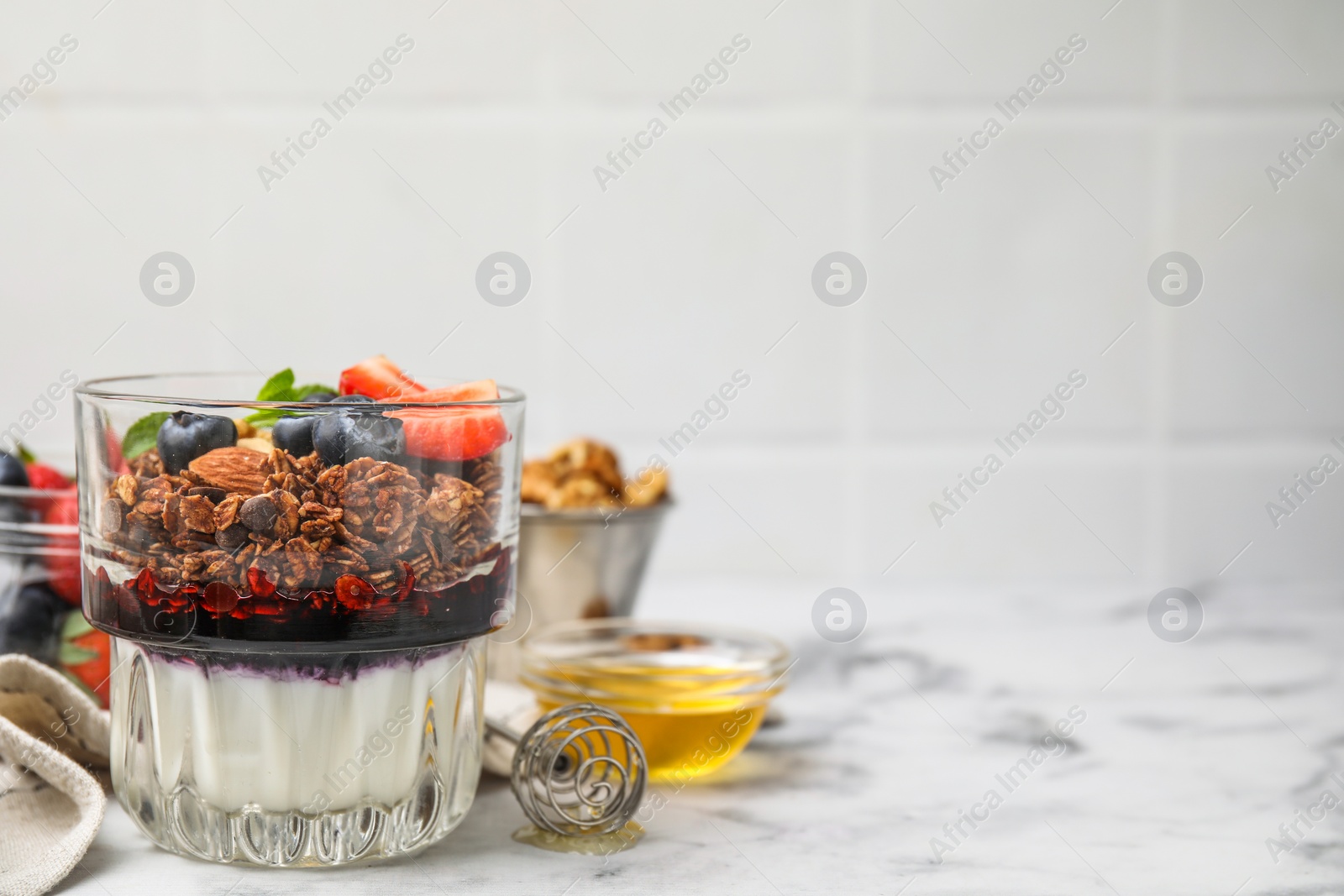 Photo of Tasty granola with berries, jam and yogurt in glass on white marble table, space for text