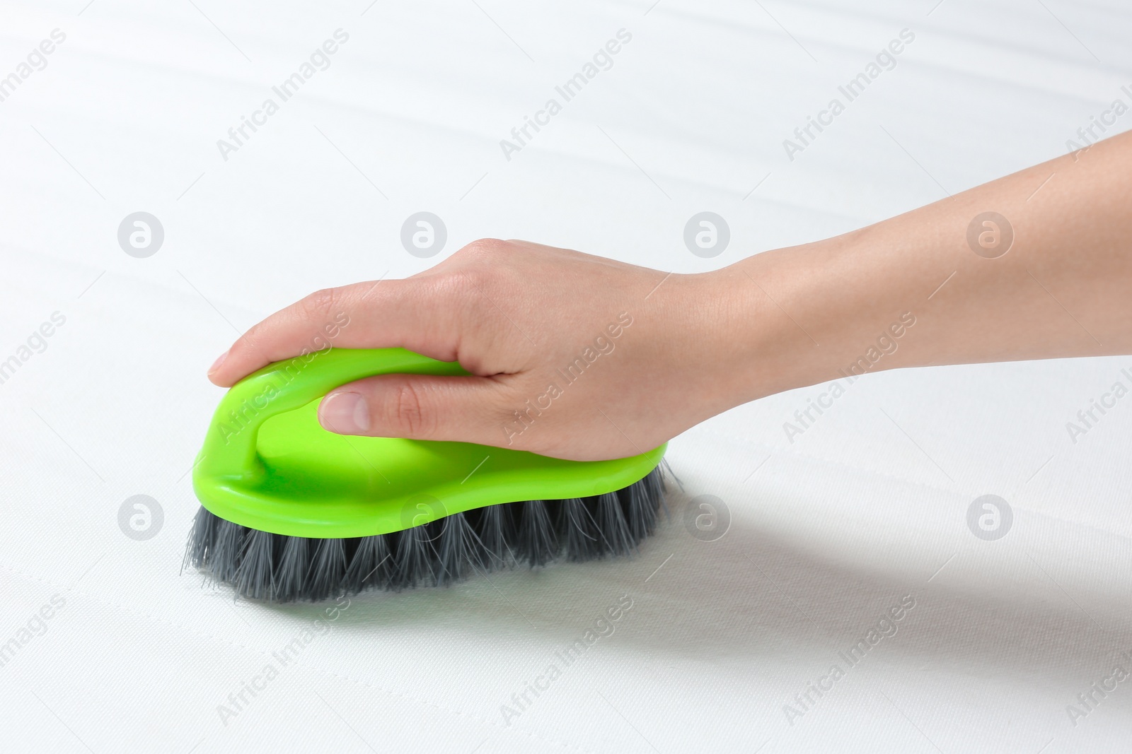 Photo of Woman cleaning white mattress with brush, closeup