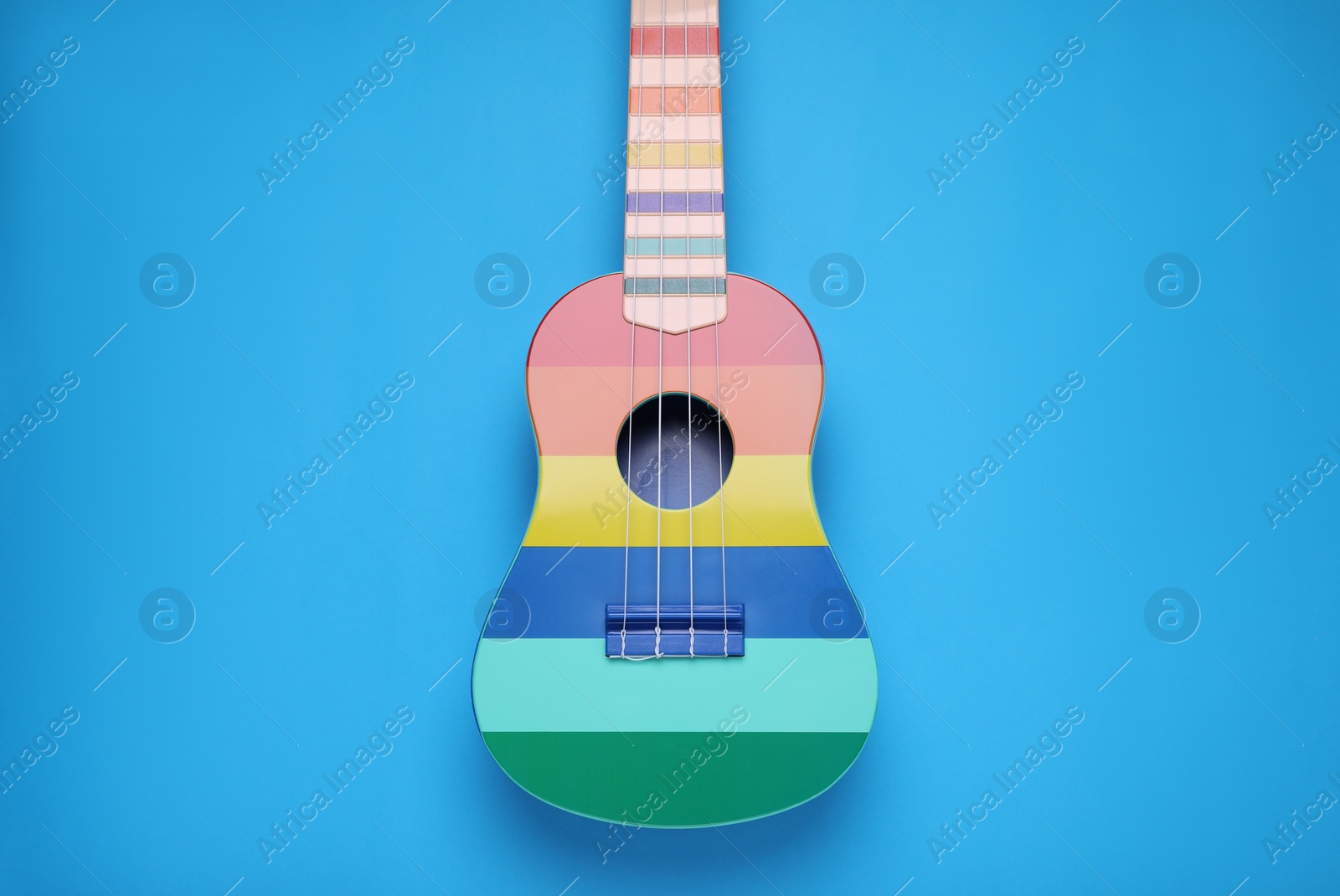 Photo of Colorful ukulele on light blue background, top view. String musical instrument