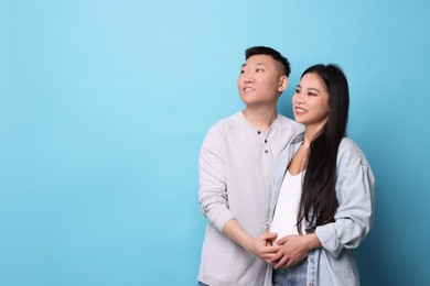 Photo of Pregnant woman and her husband on light blue background, space for text