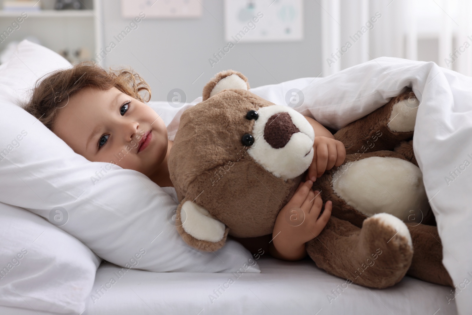 Photo of Cute little girl lying with teddy bear on bed at home