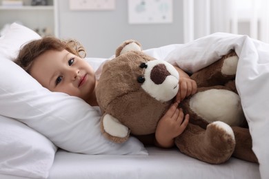 Cute little girl lying with teddy bear on bed at home