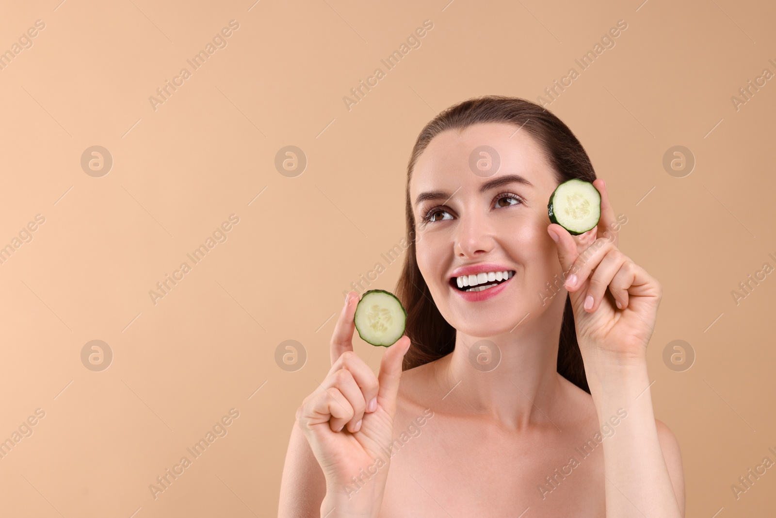 Photo of Beautiful woman with pieces of cucumber on beige background, space for text