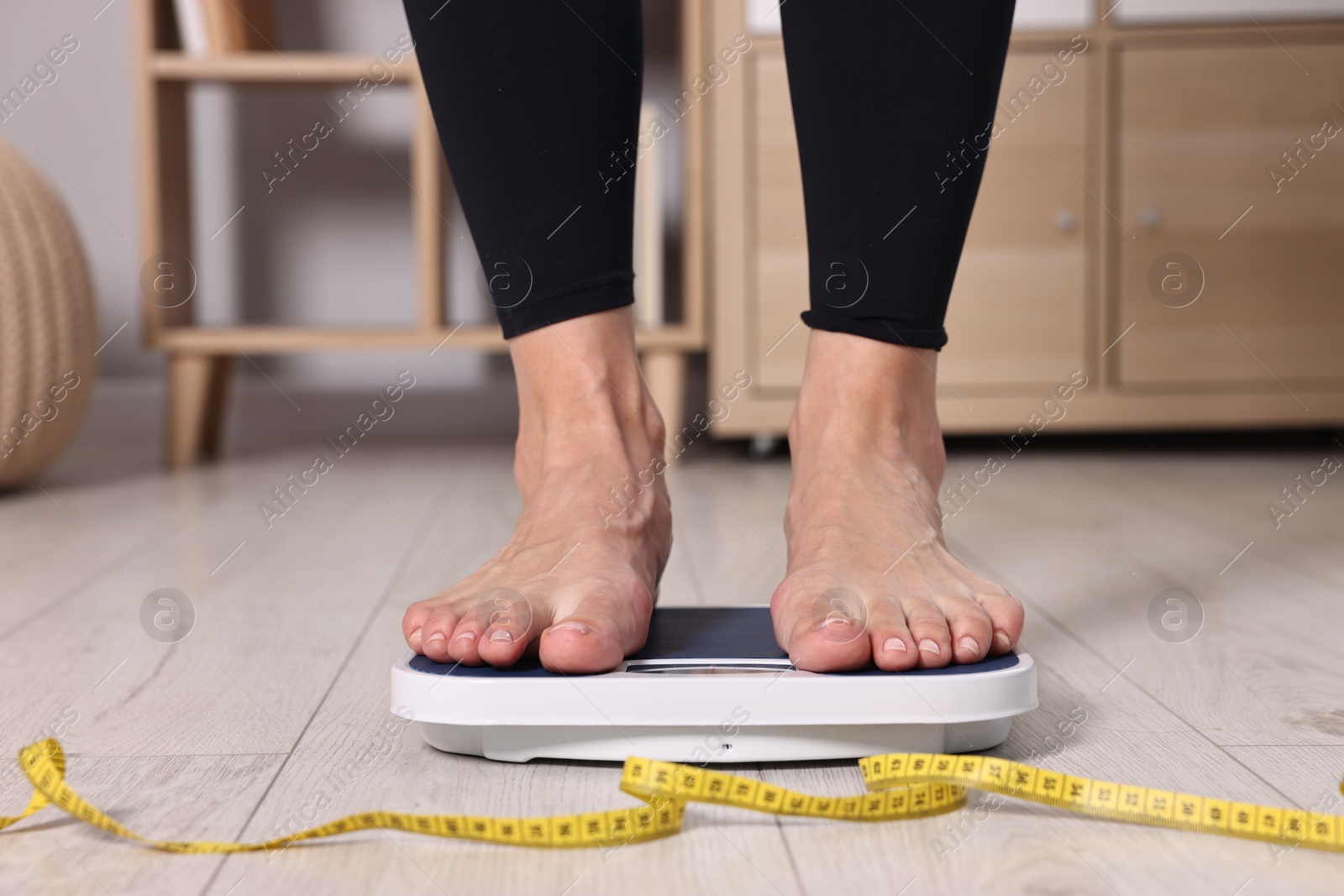 Photo of Woman standing on floor scale and measuring tape at home, closeup. Weight control