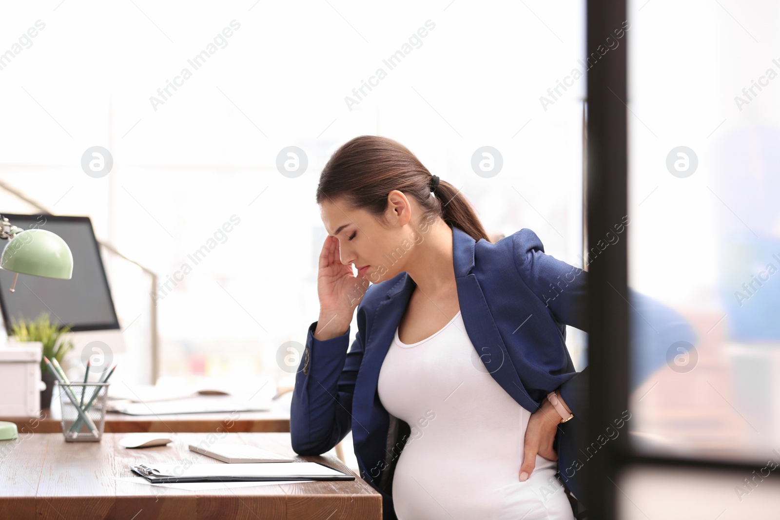 Photo of Young pregnant woman suffering from pain while working in office