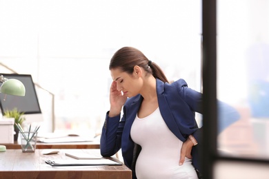 Young pregnant woman suffering from pain while working in office