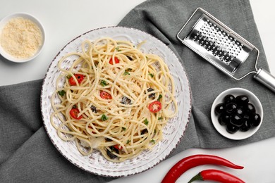 Photo of Plate of delicious pasta with olives, tomatoes and parmesan cheese near ingredients on white table, flat lay