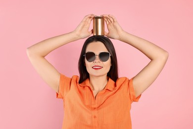 Beautiful young woman holding tin can with beverage on pink background