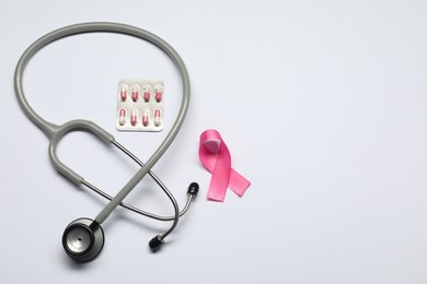 Breast cancer awareness. Pink ribbon, stethoscope and pills on white background, flat lay. Space for text