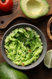 Delicious guacamole and ingredients on wooden table, flat lay