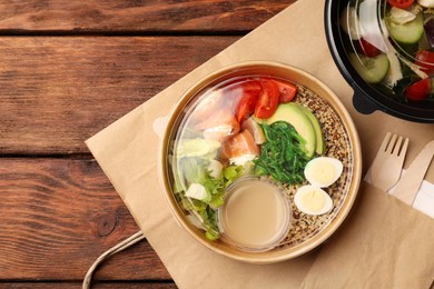 Tasty food in containers with knife and fork on wooden table, flat lay. Space for text