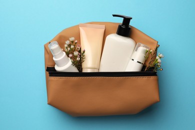 Preparation for spa. Compact toiletry bag with different cosmetic products and flowers on light blue background, top view