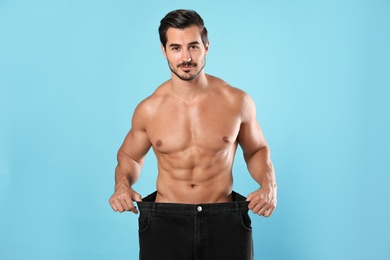 Photo of Young man with slim body in old big size jeans on light blue background