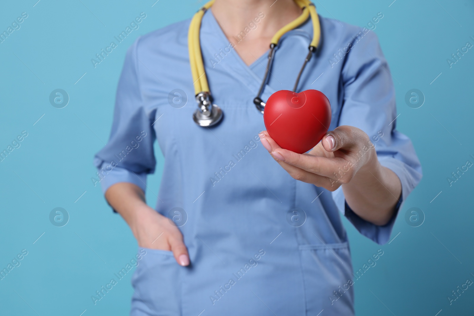 Photo of Doctor with stethoscope and red heart on light blue background, closeup. Cardiology concept