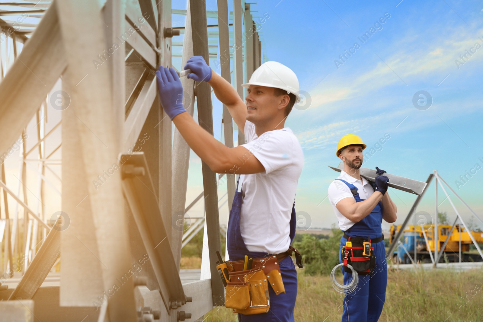 Photo of Workers building high voltage tower construction outdoors. Installation of electrical substation