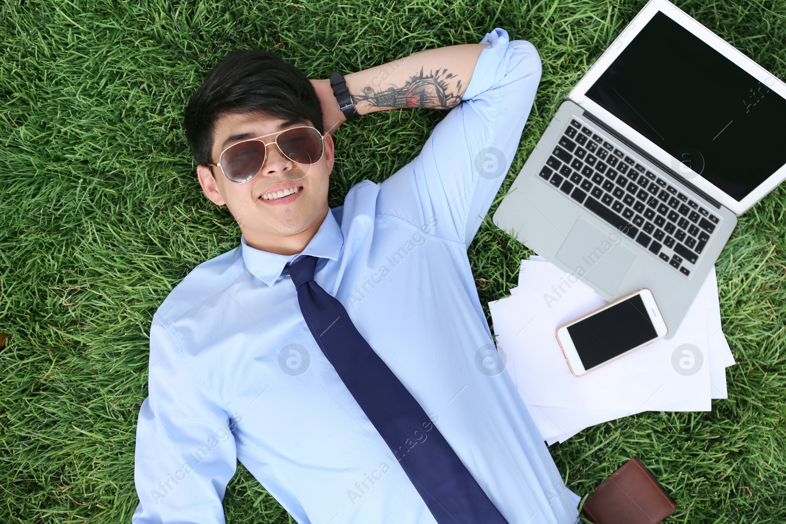 Photo of Young man lying on green lawn in park, top view. Joy in moment