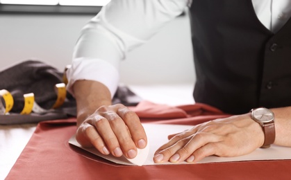 Photo of Tailor working with cloth at table in atelier