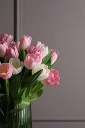 Beautiful bouquet of tulips in glass vase against grey wall