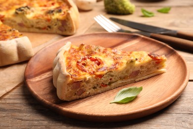 Photo of Piece of delicious homemade vegetable quiche on wooden plate, closeup