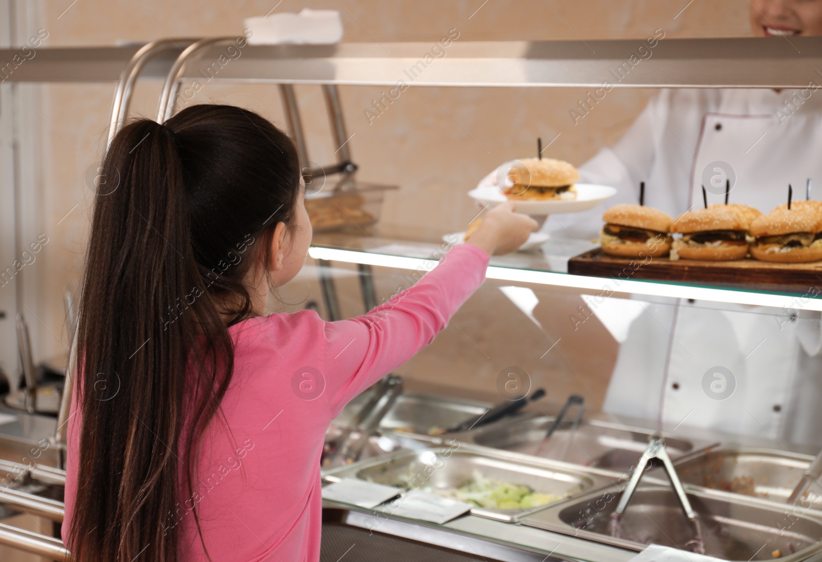 Photo of Woman giving plate with tasty food to girl in school canteen