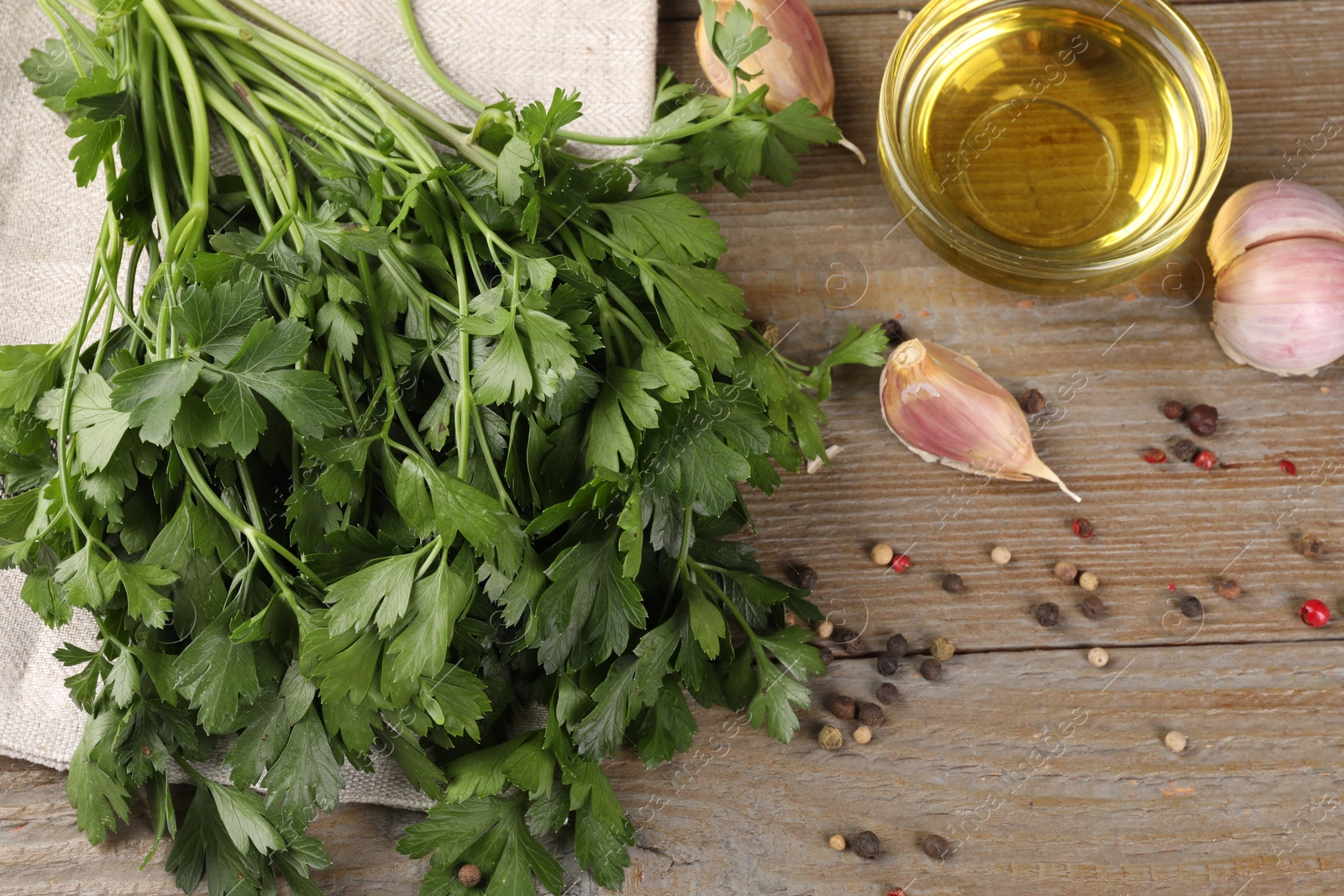 Photo of Bunch of raw parsley, oil, garlic and peppercorns on wooden table, above view