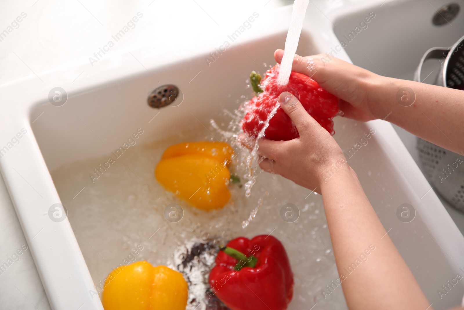 Photo of Woman washing fresh bell peppers in kitchen sink, closeup