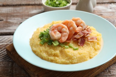 Photo of Plate with fresh tasty shrimps, bacon, grits and green onion on wooden table, closeup
