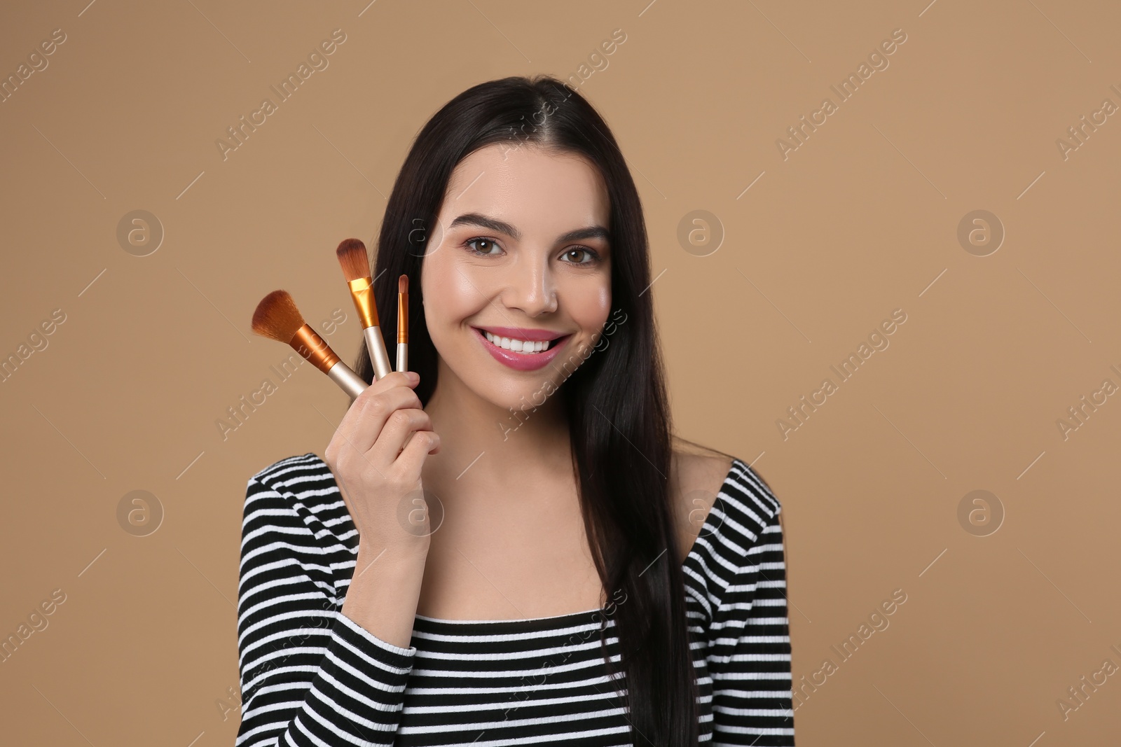 Photo of Happy woman with different makeup brushes on light brown background. Space for text