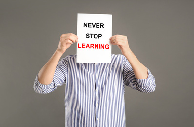 Man holding paper with phrase NEVER STOP LEARNING on grey background