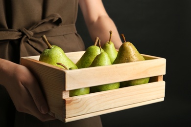 Photo of Woman holding wooden crate with ripe pears on black background, closeup