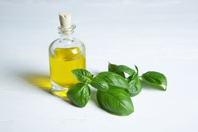 Photo of Glass bottle with oil and basil leaves on light table