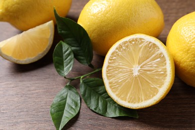 Photo of Fresh lemons and green leaves on wooden table, closeup