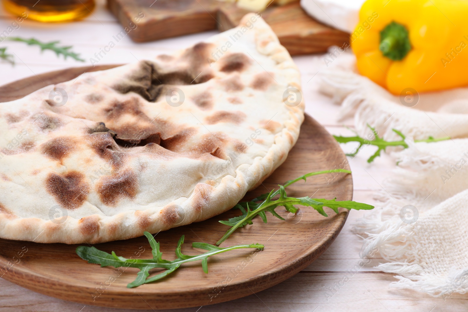 Photo of Delicious calzone on light wooden table, closeup