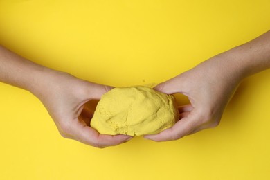 Photo of Woman playing with kinetic sand on yellow background, top view