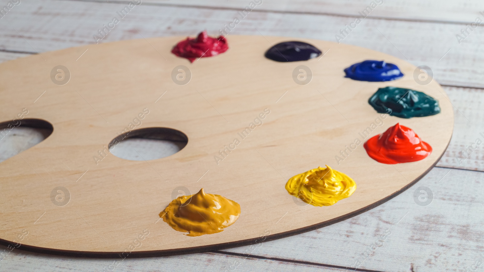 Photo of Artist's palette with samples of colorful paints on white wooden table, closeup
