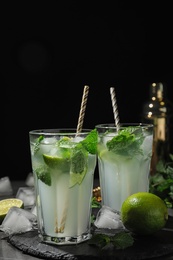 Glasses of delicious Mojito cocktail with ice and mint on grey table against black background