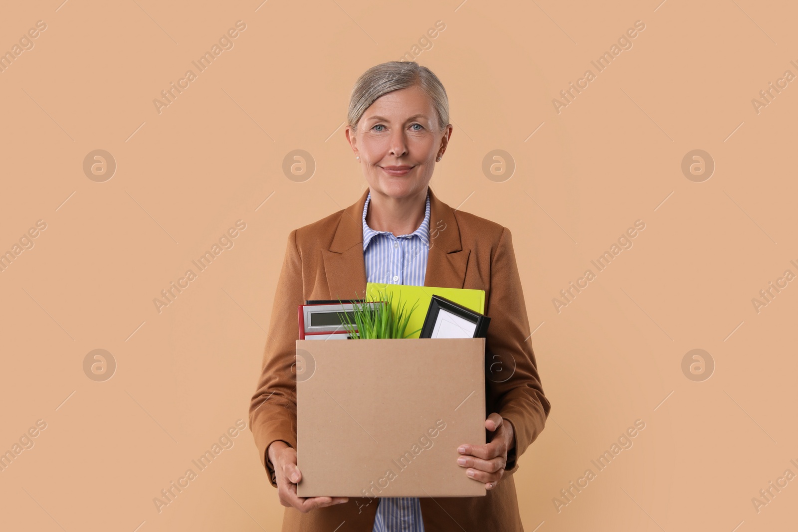 Photo of Happy unemployed senior woman with box of personal office belongings on beige background