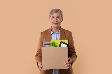 Photo of Happy unemployed senior woman with box of personal office belongings on beige background