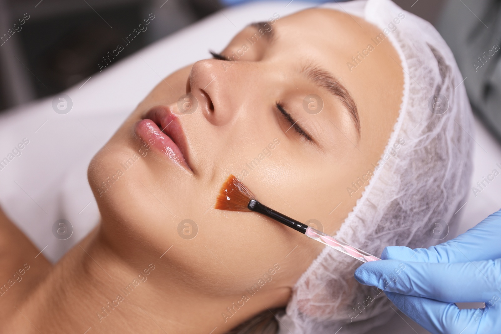 Photo of Cosmetologist applying chemical peel product on client's face in salon, closeup