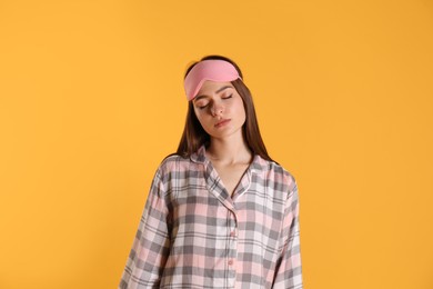 Photo of Young woman wearing pajamas and mask in sleepwalking state on yellow background