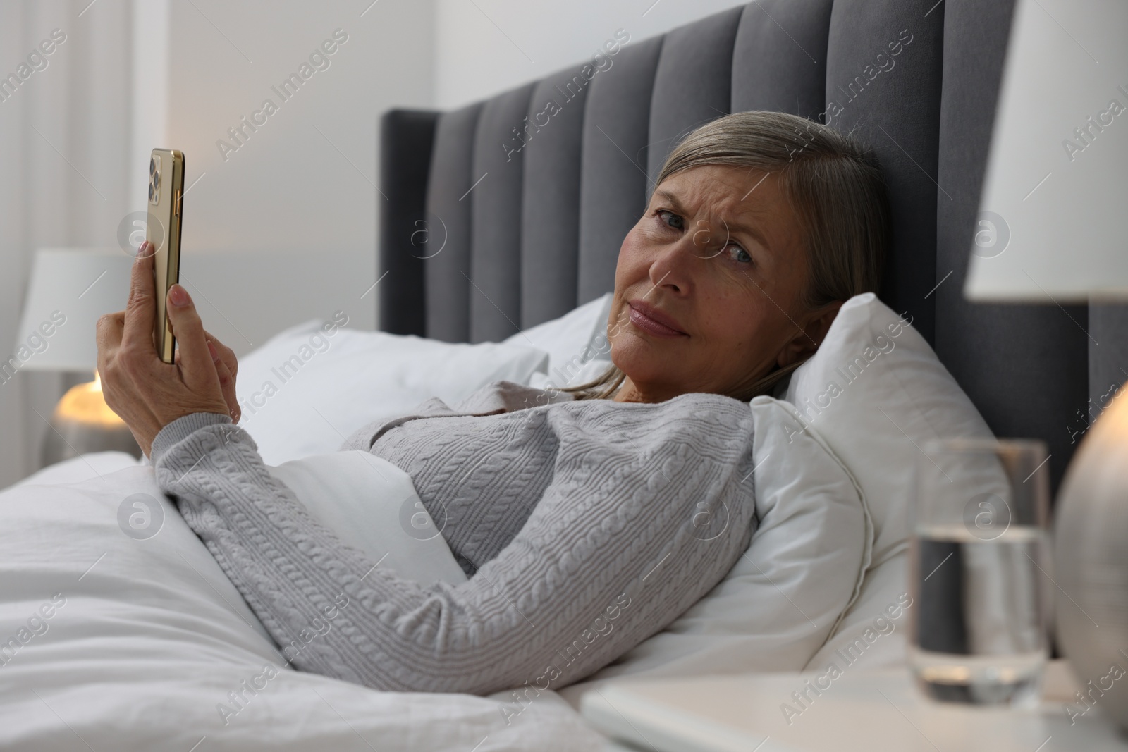 Photo of Menopause. Sleepless woman using smartphone in bed indoors