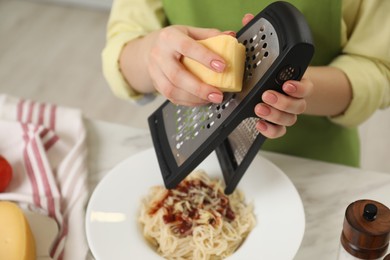 Photo of Woman grating cheese onto delicious pasta at white marble table indoors, closeup
