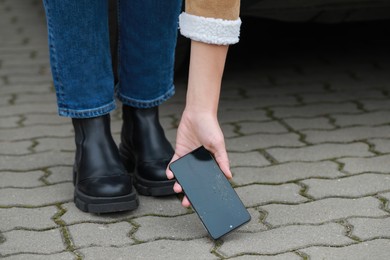 Photo of Woman taking dropped smartphone from pavement, closeup. Device repairing