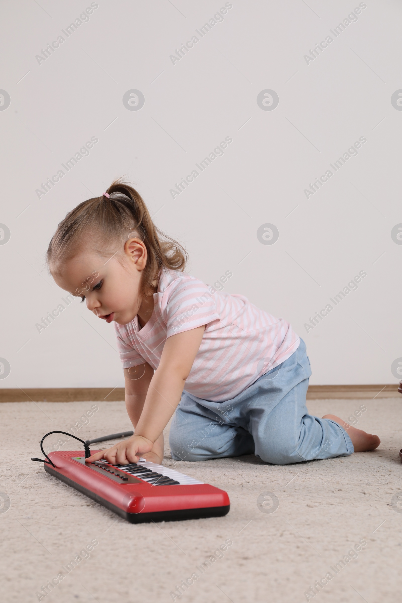 Photo of Cute little girl playing with toy piano at home