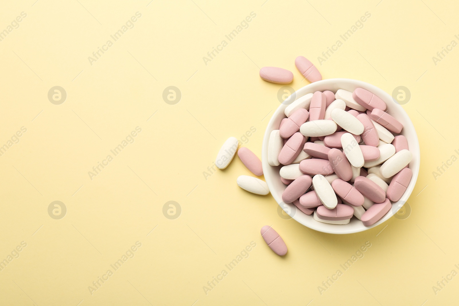 Photo of Different vitamin pills in bowl on pale yellow background, top view. Space for text