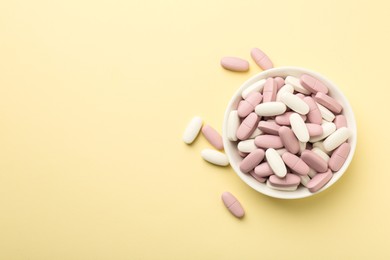 Different vitamin pills in bowl on pale yellow background, top view. Space for text